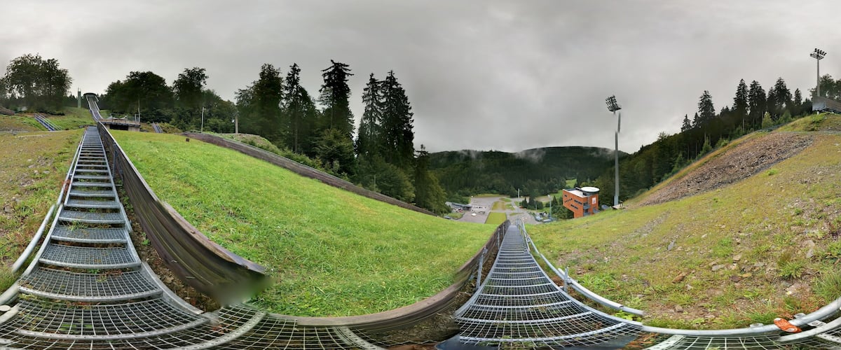 A series of metal spiral staircases leading up a grassy hill with trees in the background.