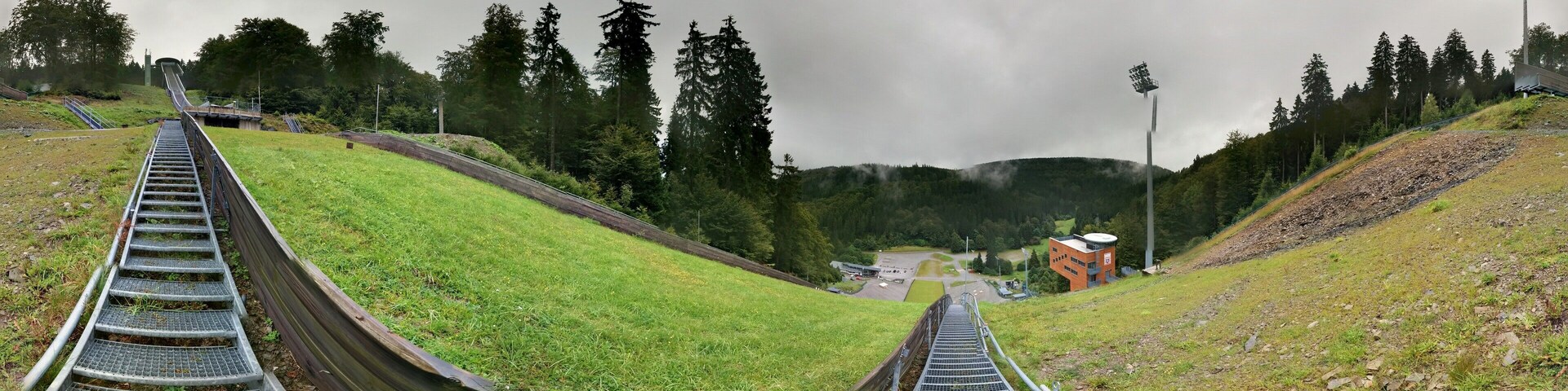 A series of metal spiral staircases leading up a grassy hill with trees in the background.