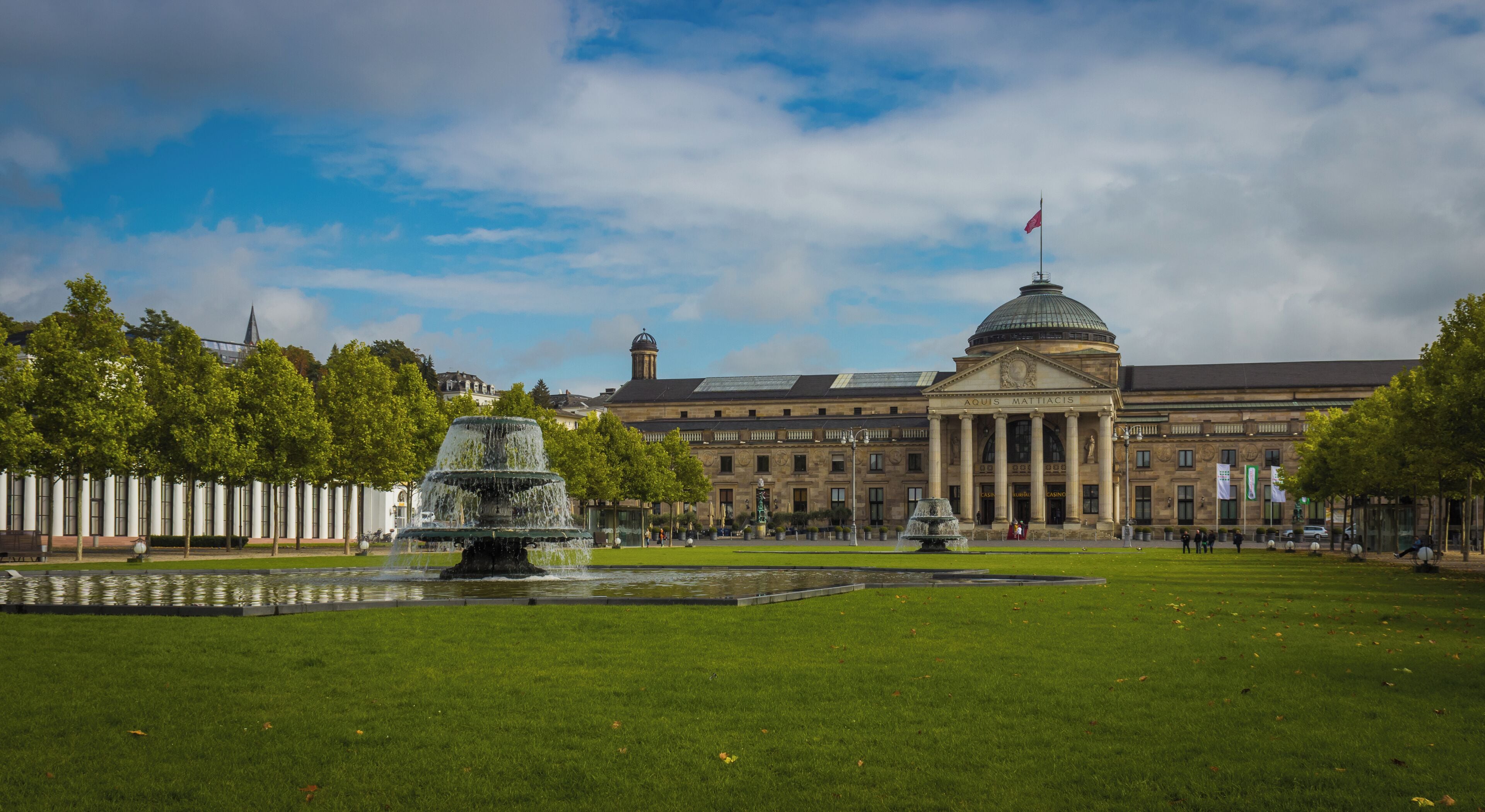 A large building with a dome and columns, a fountain, and a well-maintained lawn.