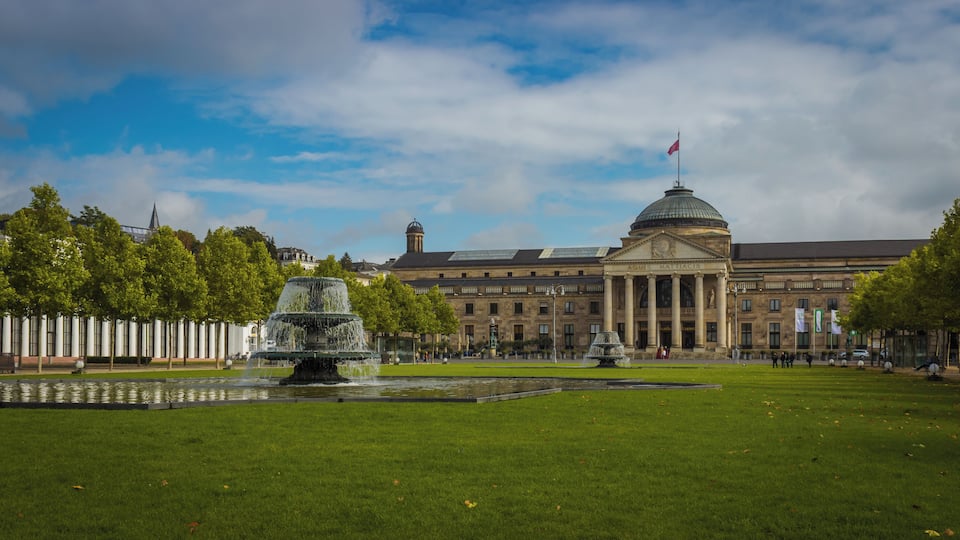 A large building with a dome and columns, a fountain, and a well-maintained lawn.