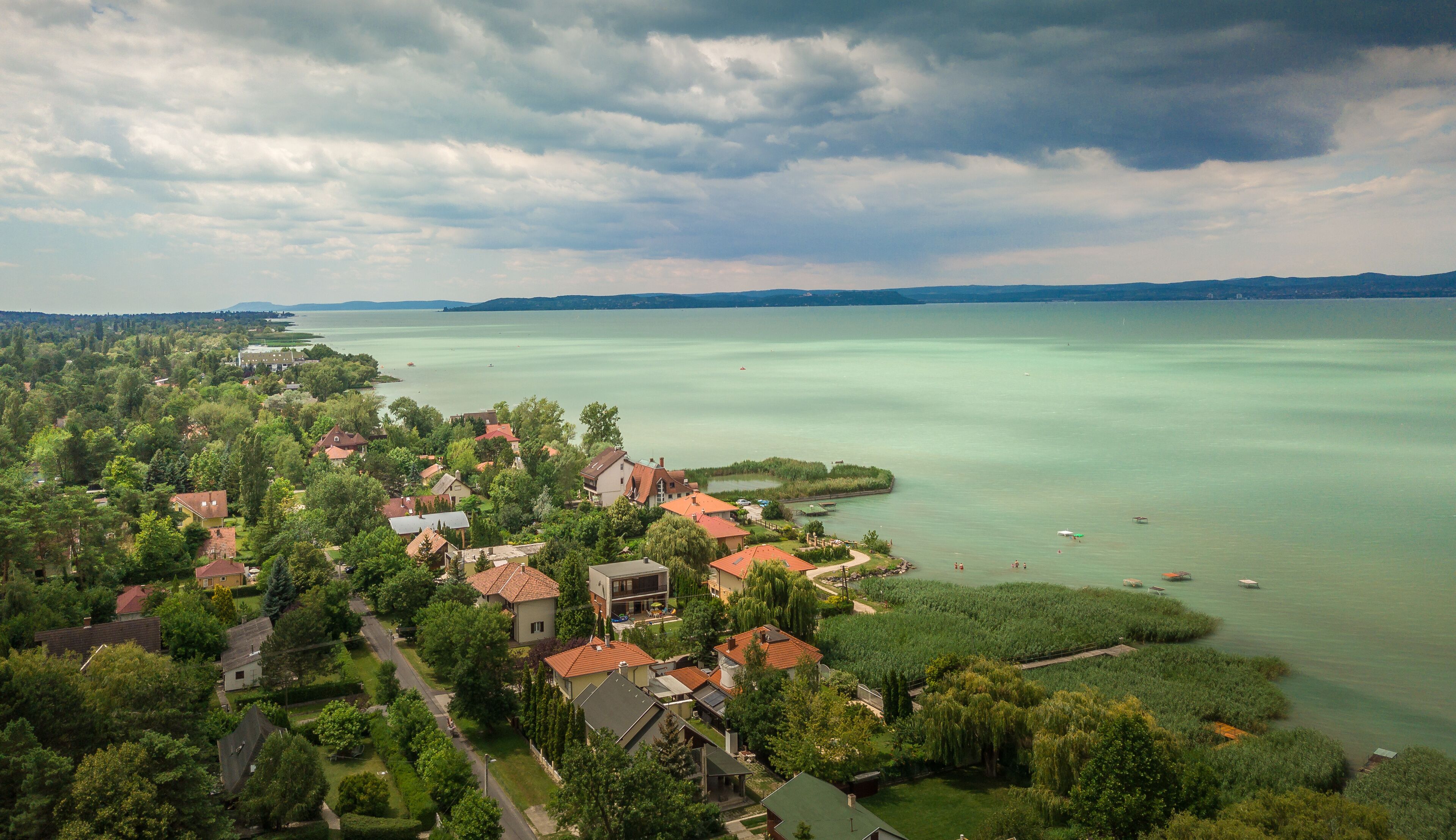 Aerial view of green water of Lake Balaton popular summer vacation spot at Balatonszeplak and Zamardi, beach houses, reed with stormy clouds brewing in Hungary
