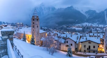 View of Church of Saint Pantalon and the snow covered town centre and mountainous background in winter, Courmayeur, Aosta Valley
