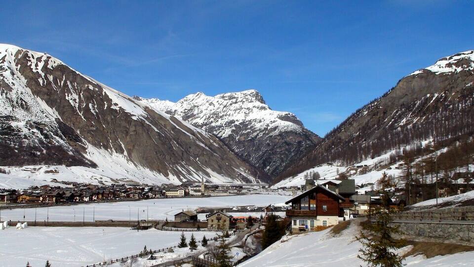 A snow-covered mountain village with buildings and a ski slope.