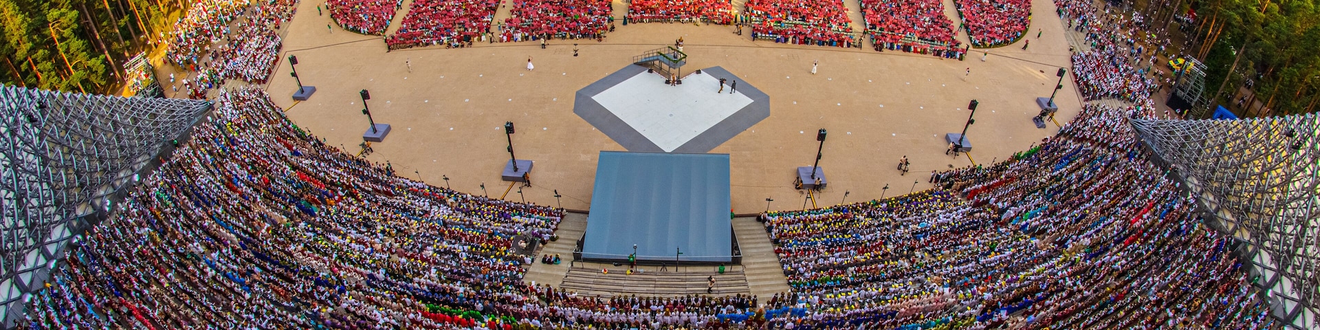 Riga, Latvia - 13 July 2025: Aerial view of Mezaparks open-air stage filled with a massive crowd of people during a large cultural event, surrounded by dense pine forest.