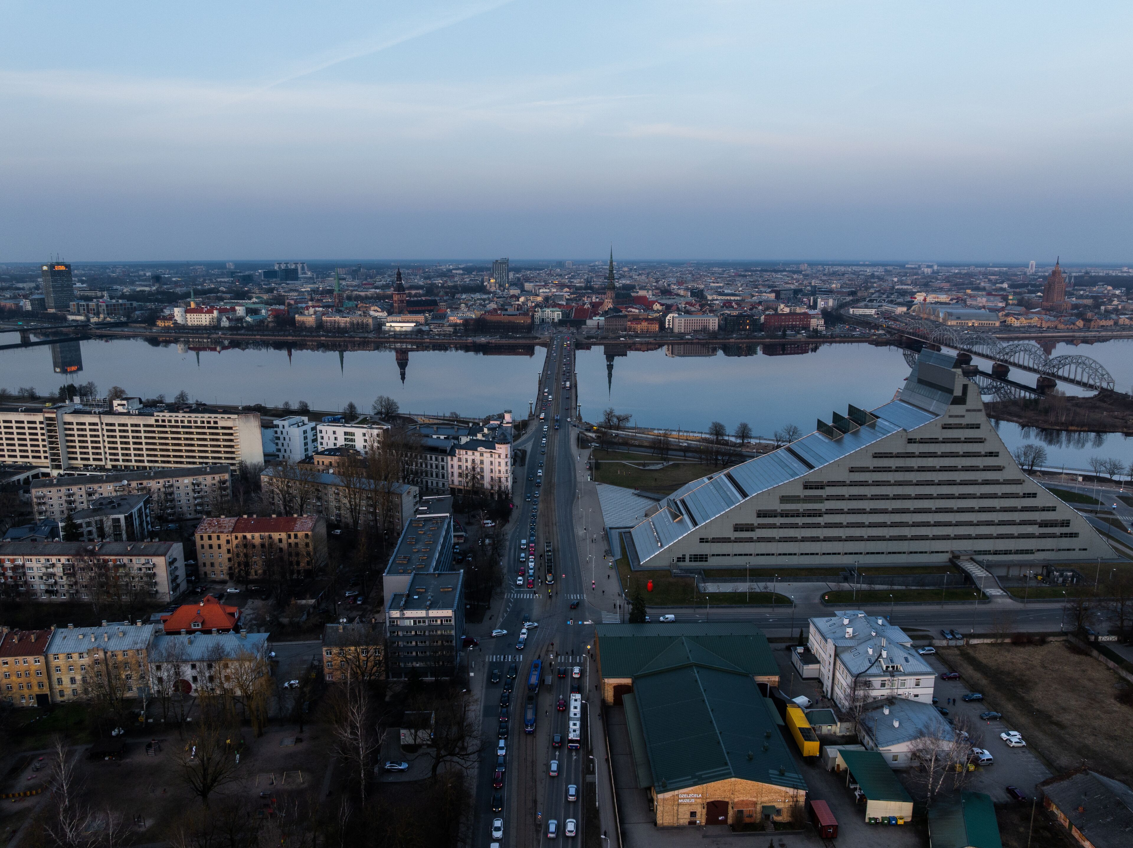 Aerial view of the National Library of Latvia and the Akmens tilts bridge spanning the Daugava River towards the historic Old Riga skyline at sunset, Riga, Latvia.