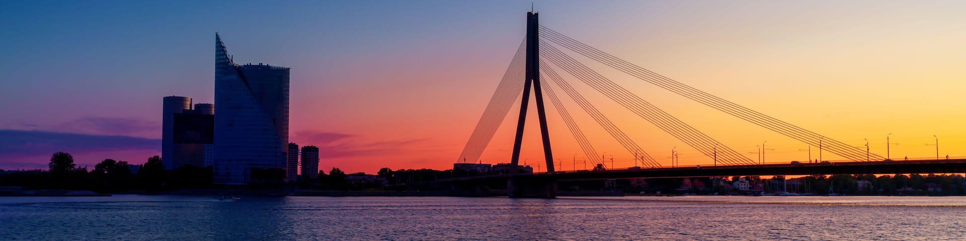 A sunset over a river with a modern bridge and a city skyline in the background.