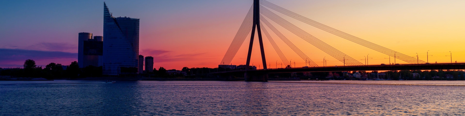 Atardecer sobre un río con un puente moderno y un horizonte urbano al fondo.