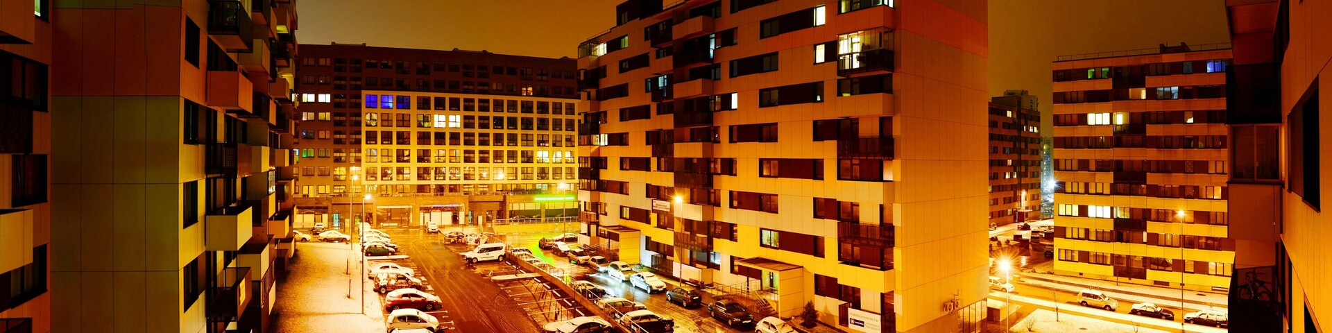 Una calle urbana nocturna con edificios de varios pisos y automóviles estacionados.