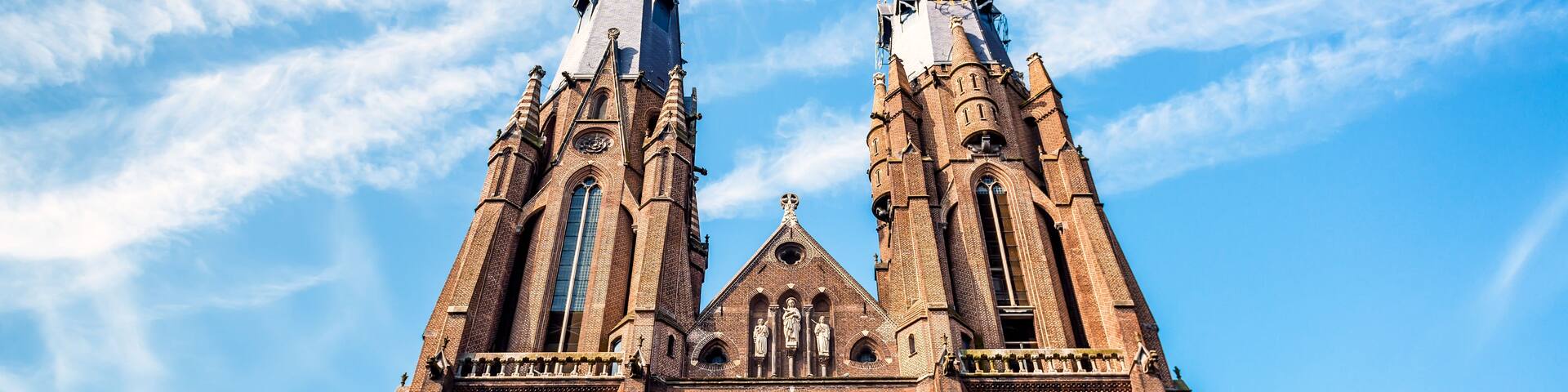 A large brick church with two tall spires and a large circular stained glass window.