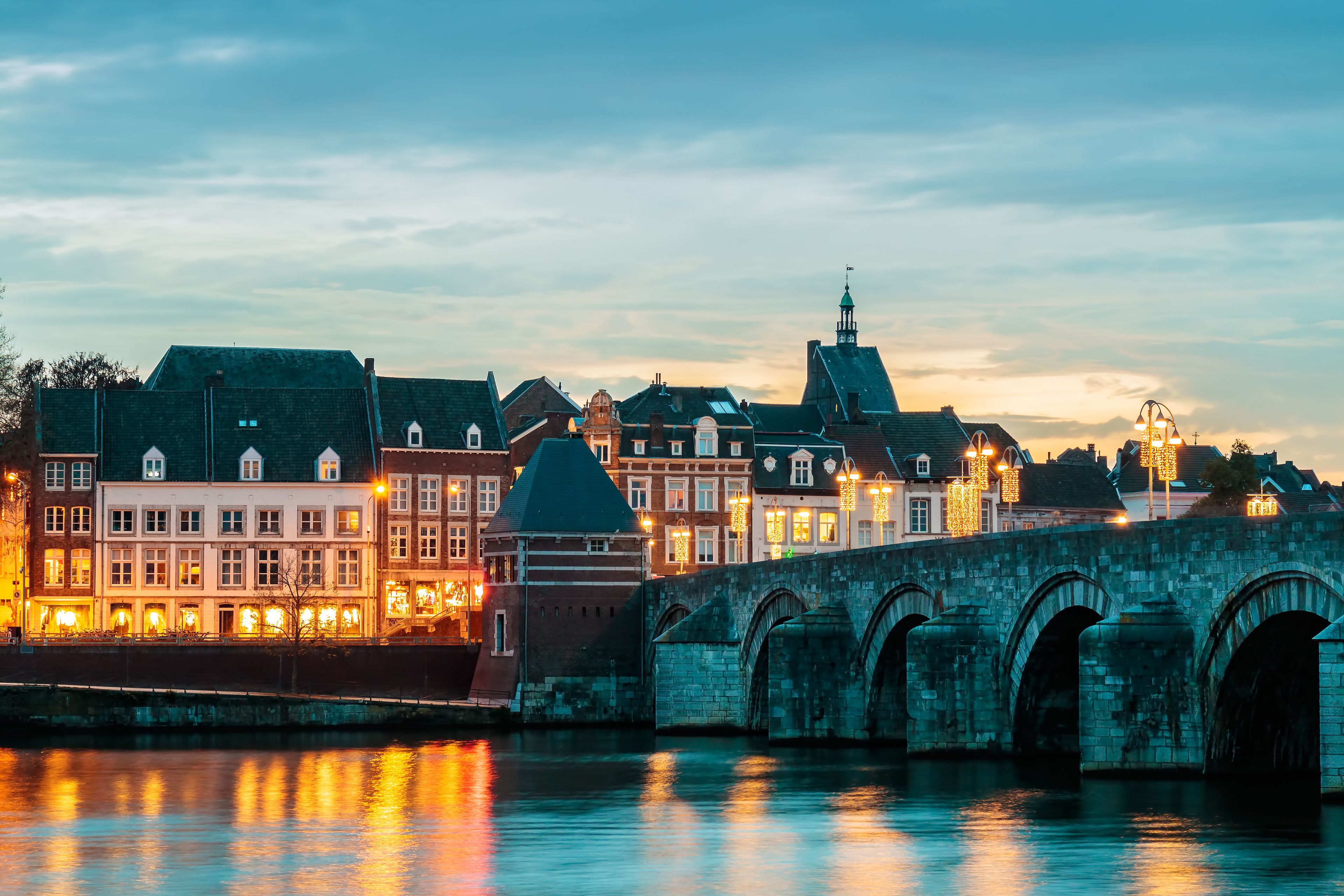 Eine historische Brücke mit mehreren Bögen über einem Fluss, der Stadtlichter reflektiert.