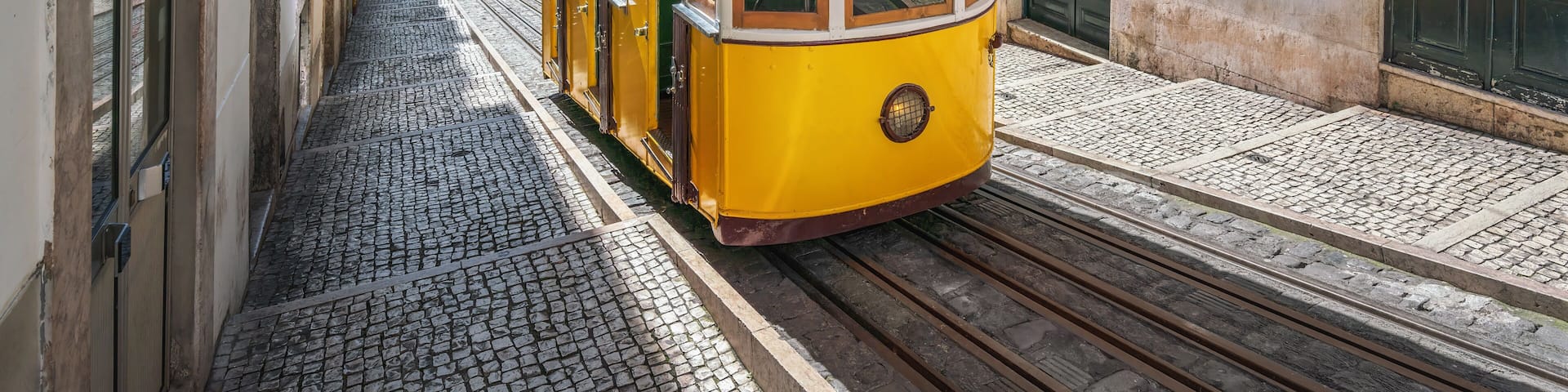 A yellow tram on a cobblestone street between buildings.