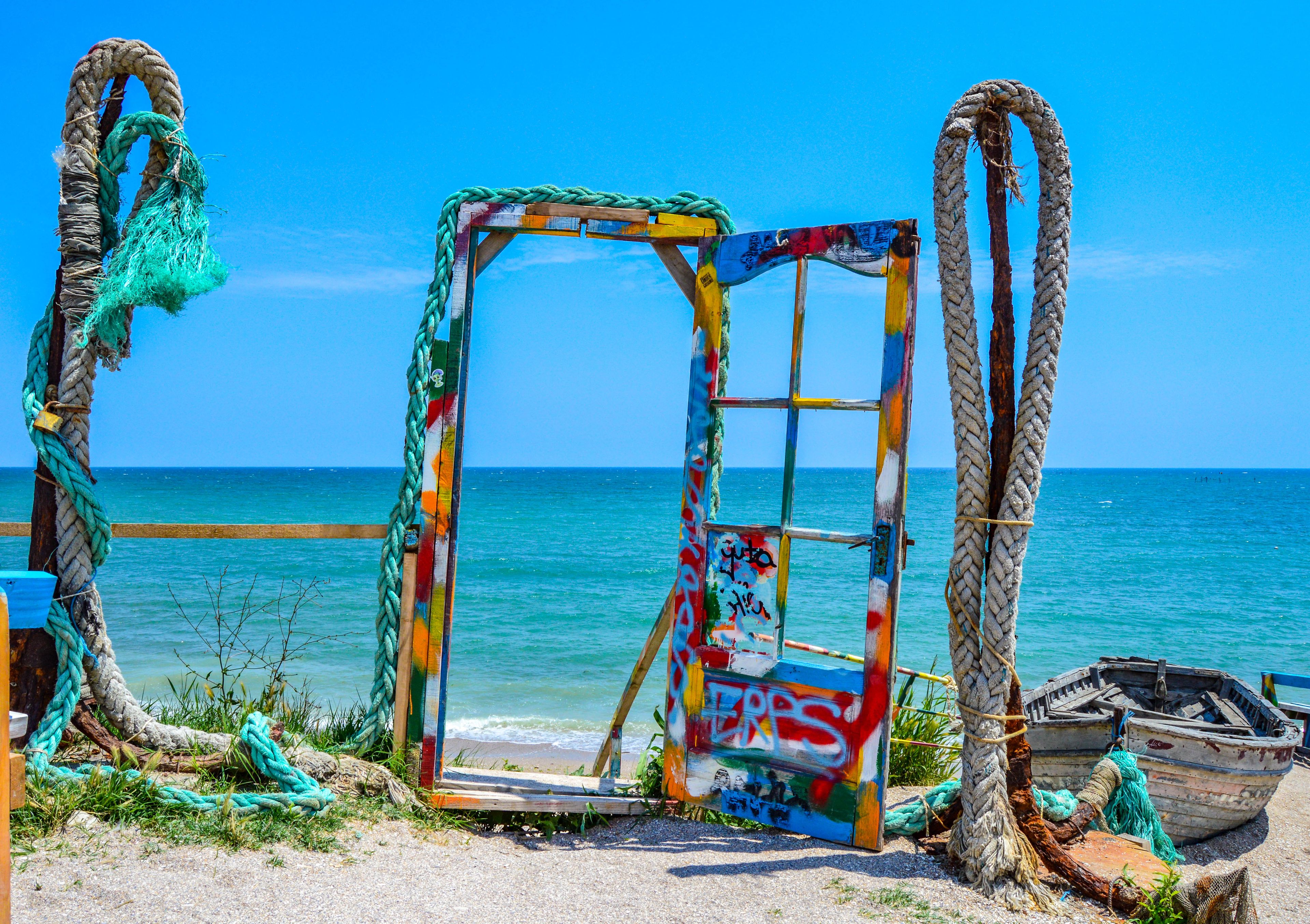 Een kleurrijke, met graffiti beschilderde metalen constructie met touwen, voor een achtergrond van strand en oceaan.