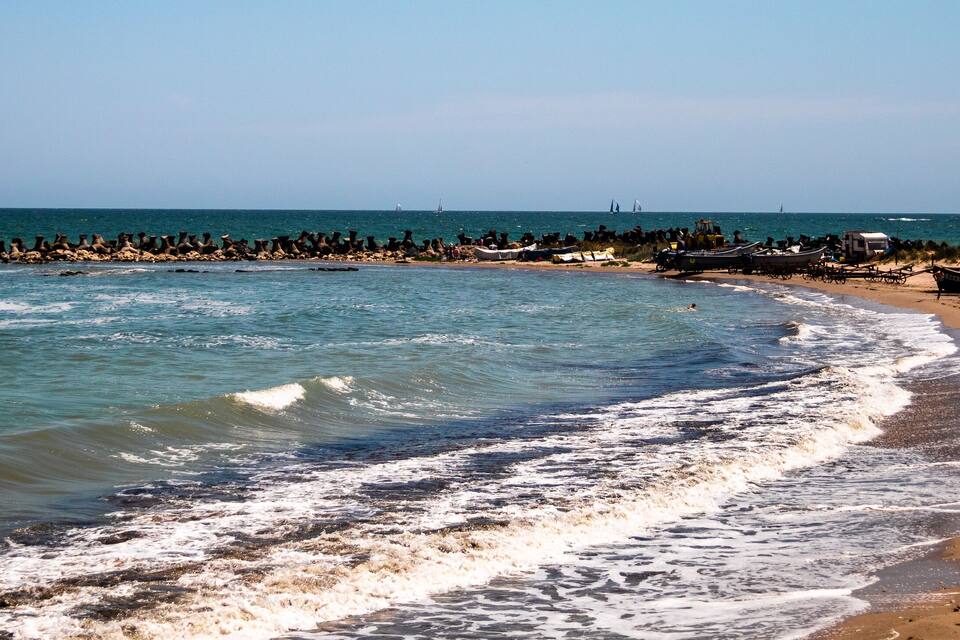 A beach with waves, boats, and a distant sailboat.