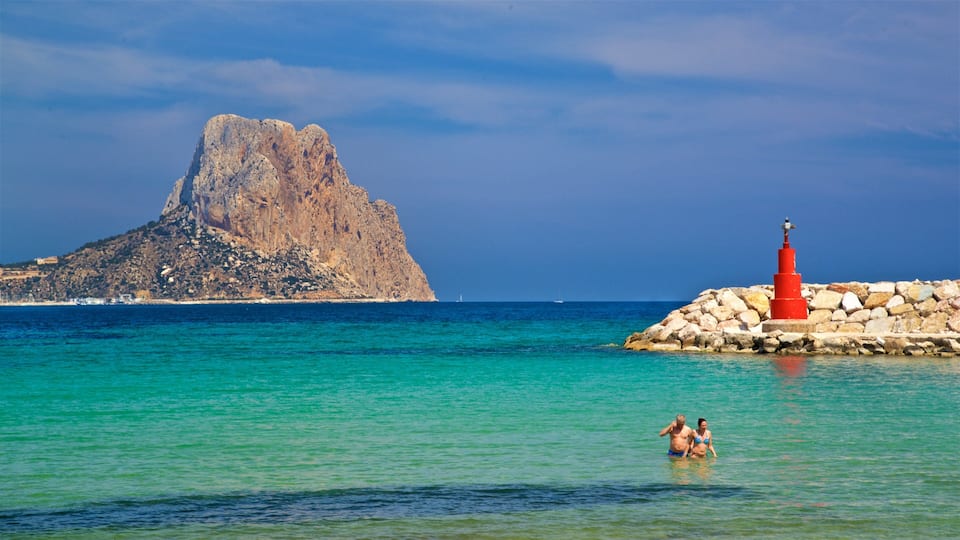 A coastal scene with a prominent rocky mountain, clear turquoise waters, and a red lighthouse on a rocky outcrop.