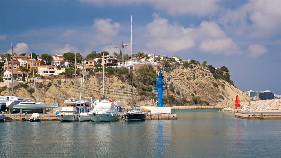 A coastal marina with boats docked, a prominent blue lighthouse, and a hillside with buildings.