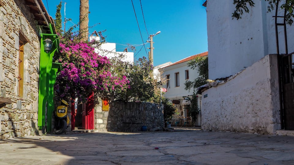 A narrow street with stone buildings, a scooter, and vibrant pink bougainvillea flowers.