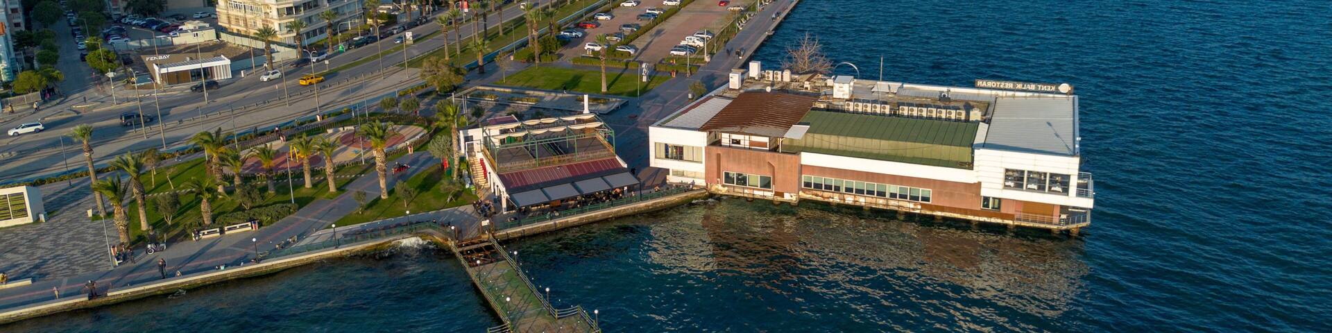A coastal cityscape with a prominent waterfront restaurant, a marina, and a dense urban area with high-rise buildings.