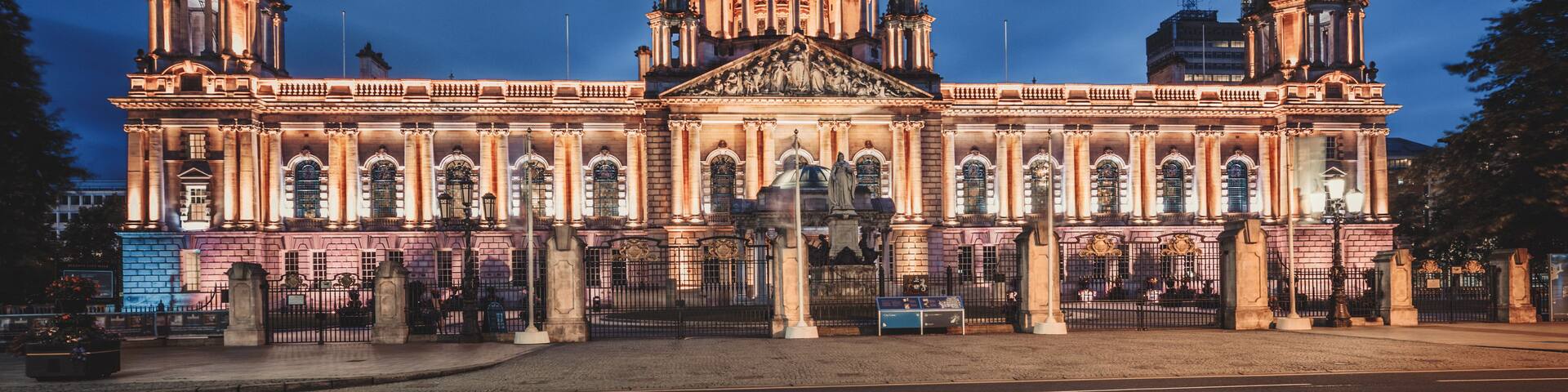 A grand neoclassical building with a large central dome and two smaller domes, illuminated at dusk.