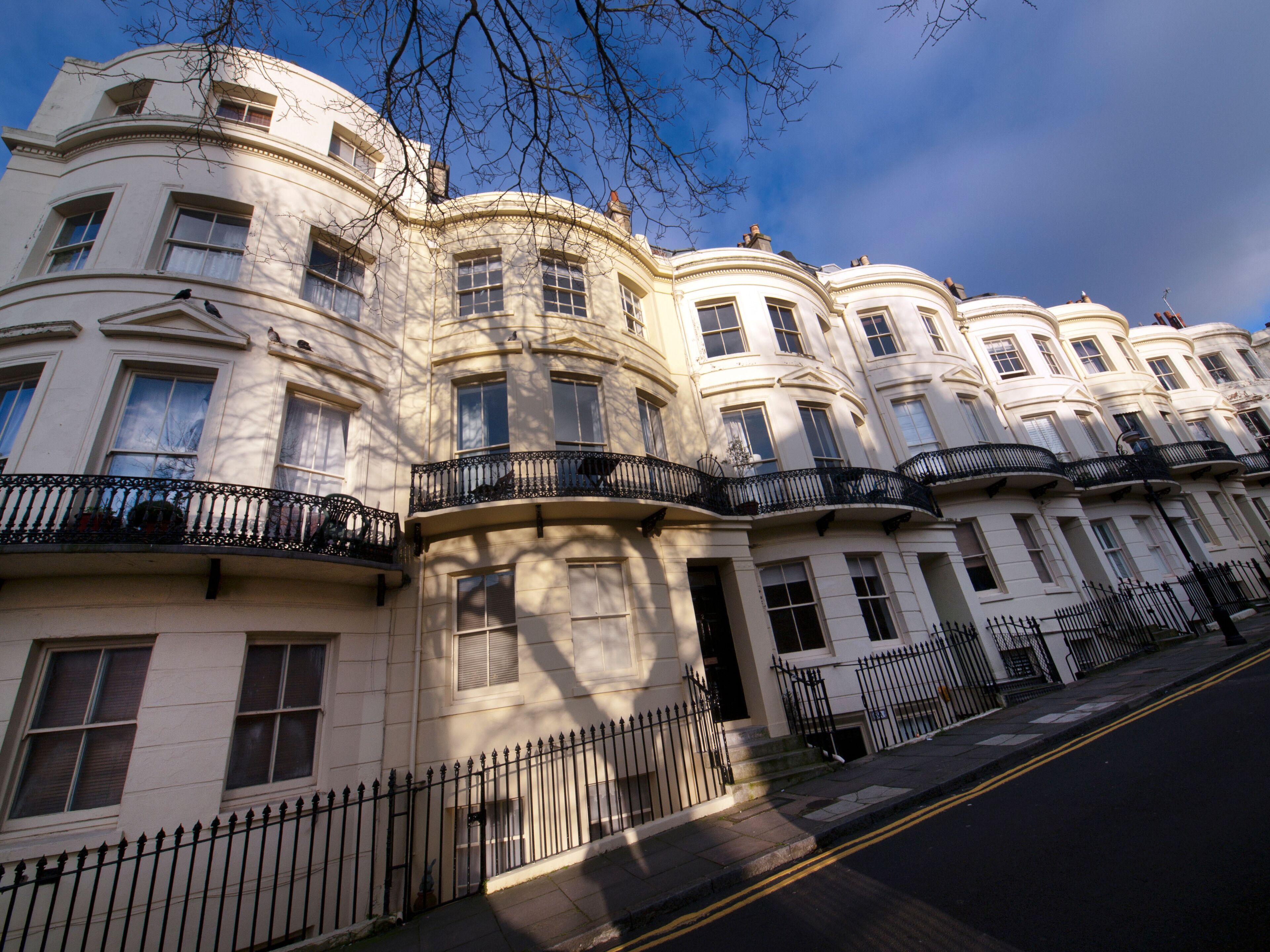 A row of white Victorian-style townhouses with black iron balconies and a clear blue sky.