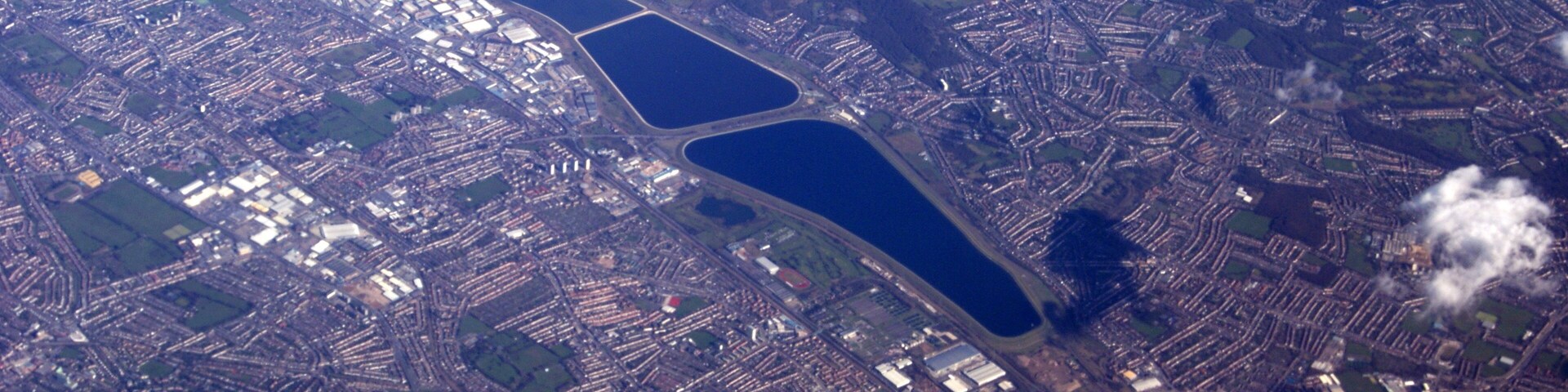 An ariel picture showing part of North London including Edmonton, Ponders End, Brimsdown, Chingford and several reservoirs in the Lee Valley Reservoir Chain. From the top of the photo are the twin basins of the King George V reservoir adjacent to the William Girling reservoir, the circular Banbury Reservoir close by to the Lockwood Reservoir. A section of Epping Forest can be seen to the top right of the photograph