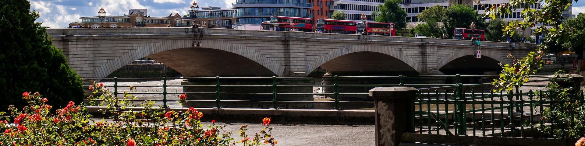 A modern bridge with arches, a river, and a red bus.