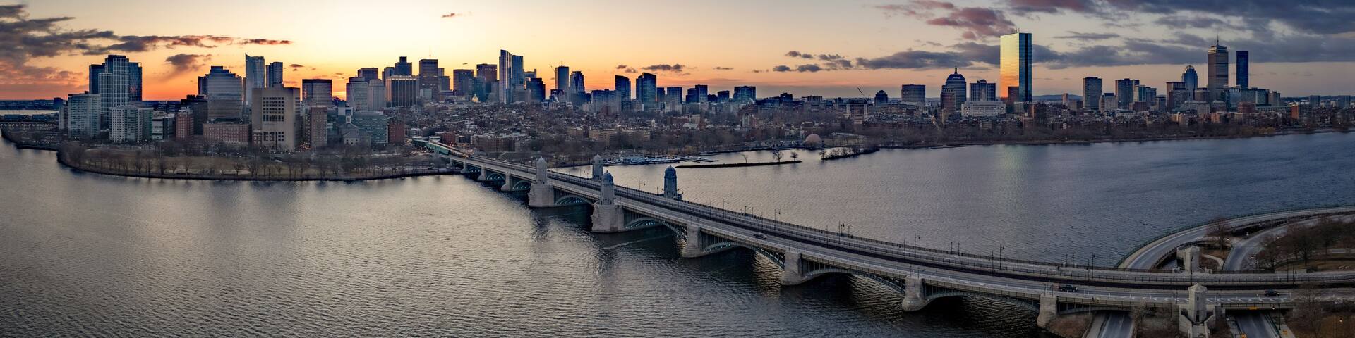 A city skyline at sunset with a prominent bridge crossing a river.