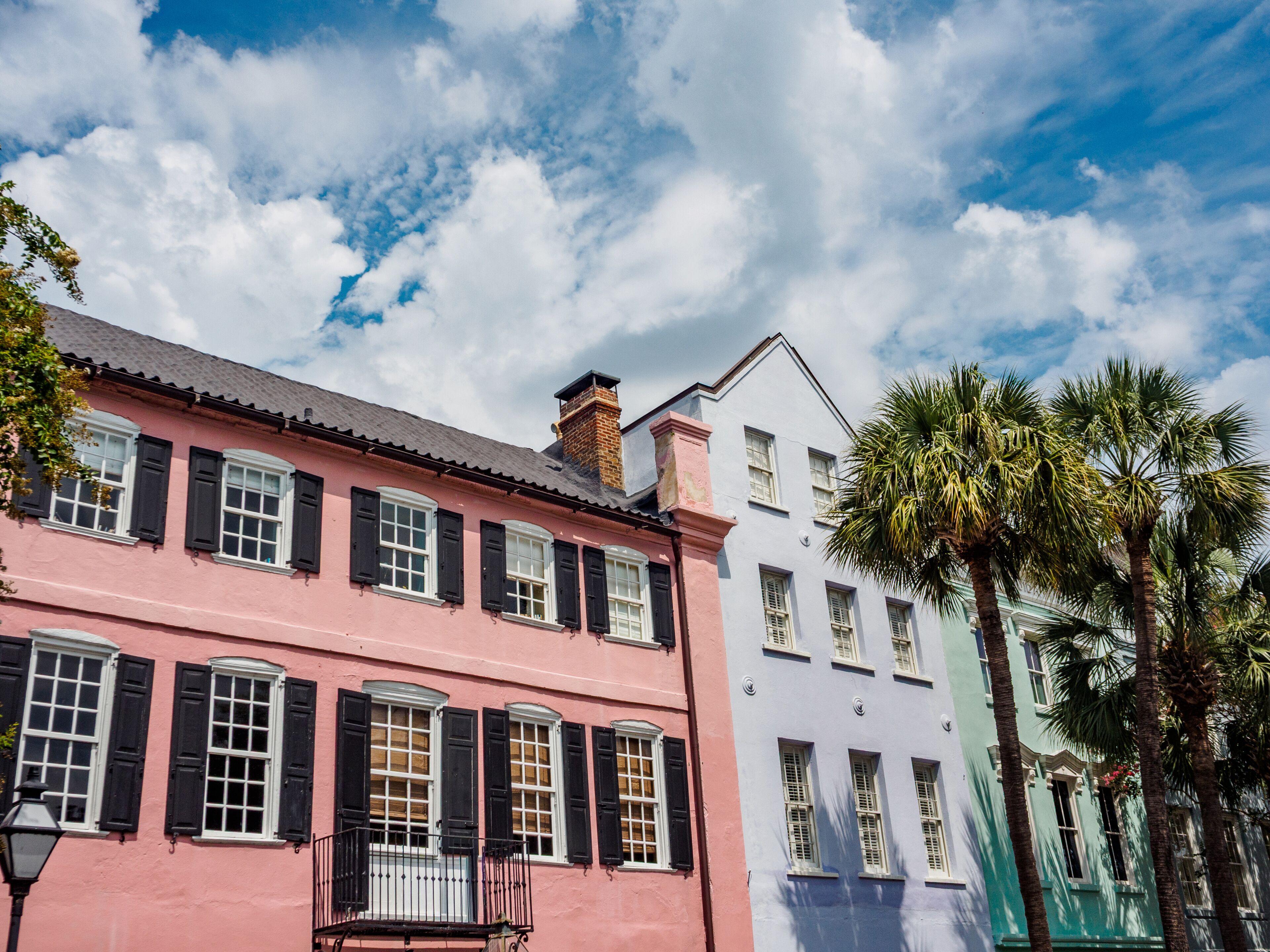 A row of colorful historic buildings with shutters, under a partly cloudy sky.