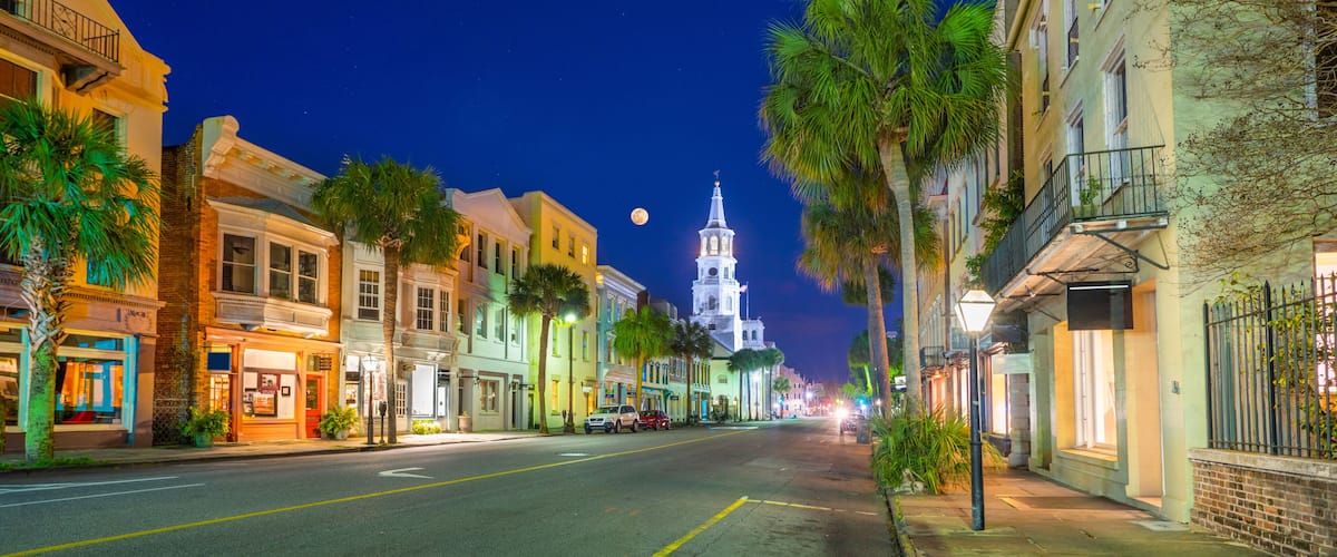 A nighttime street with historic buildings, palm trees, and a church steeple under a starry sky.