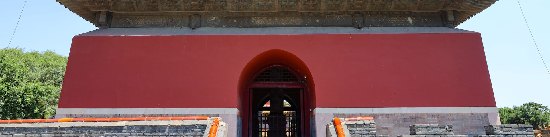 A traditional Chinese building with a red and grey facade, ornate roof with lion statues, and a central arched entrance.