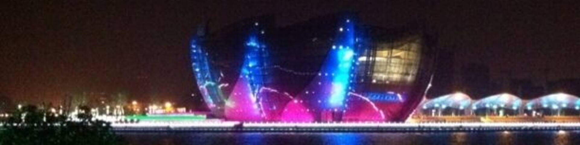 A nighttime view of a large, illuminated building with a unique, angular design by the water.