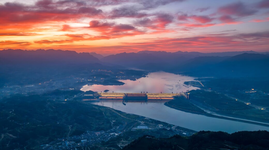 A river with a dam and surrounding mountains during sunset.