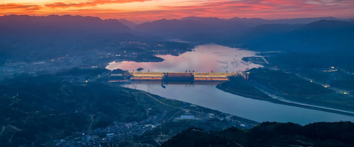 A river with a dam and surrounding mountains during sunset.