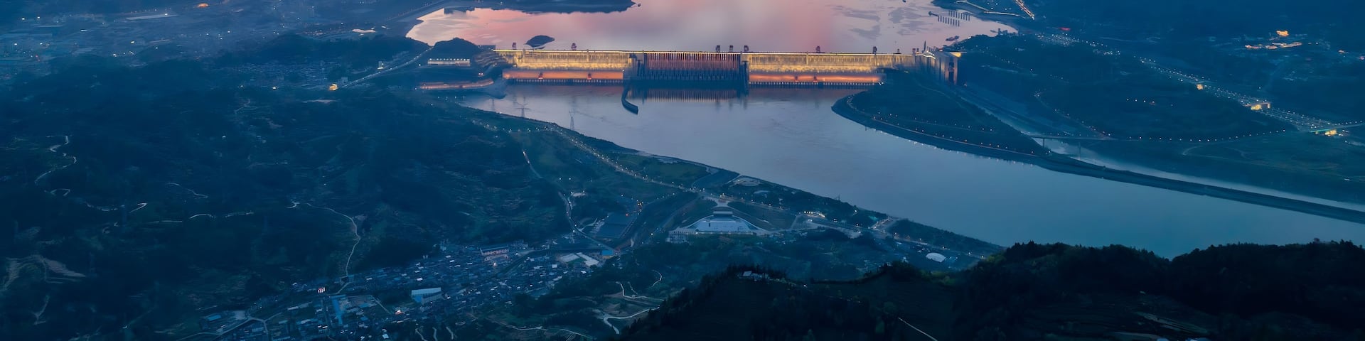 A river with a dam and surrounding mountains during sunset.