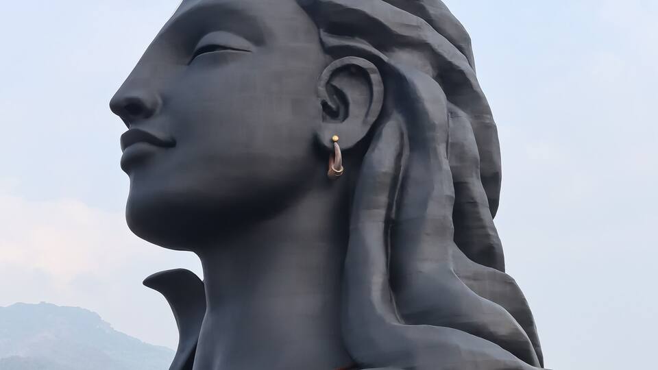 Una estàtua gran d'una figura amb una creixent lunar al cap, amb un paisatge de muntanyes al fons.