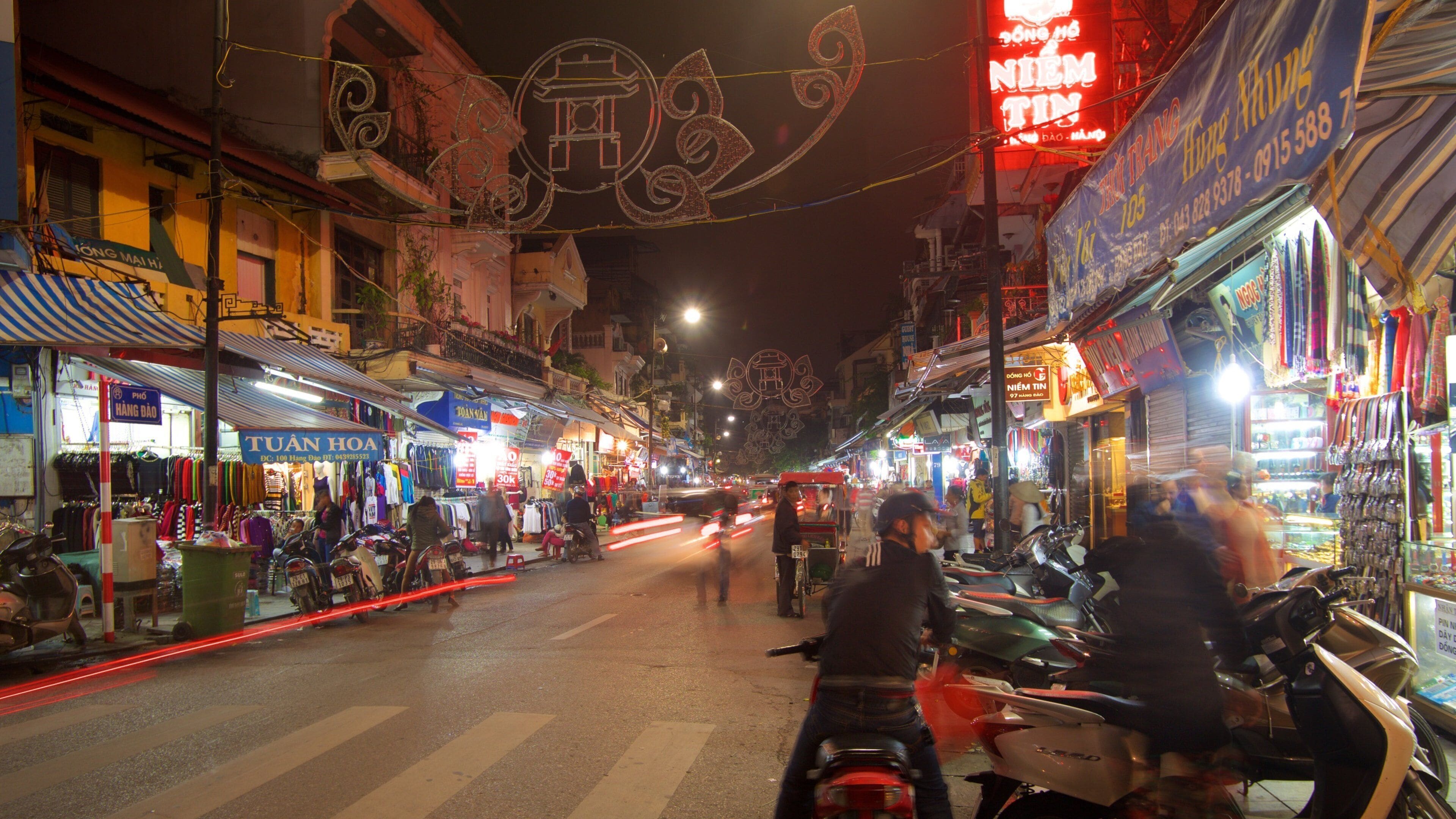 A busy street at night with shops and motorcycles.