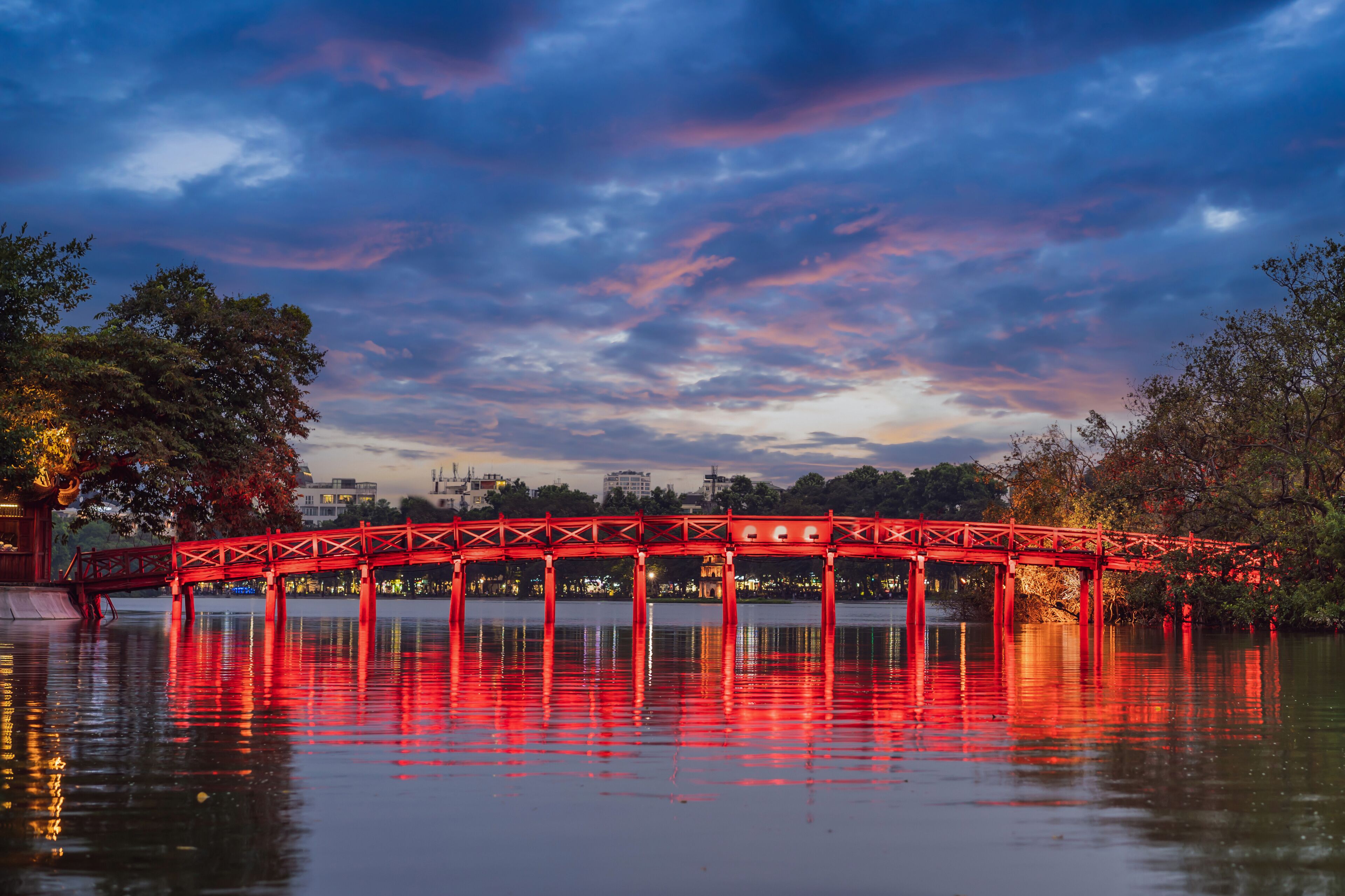 Un puente rojo sobre una masa de agua, con el horizonte de una ciudad al fondo.