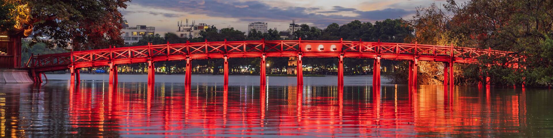 A red bridge over a body of water with a city skyline in the background.