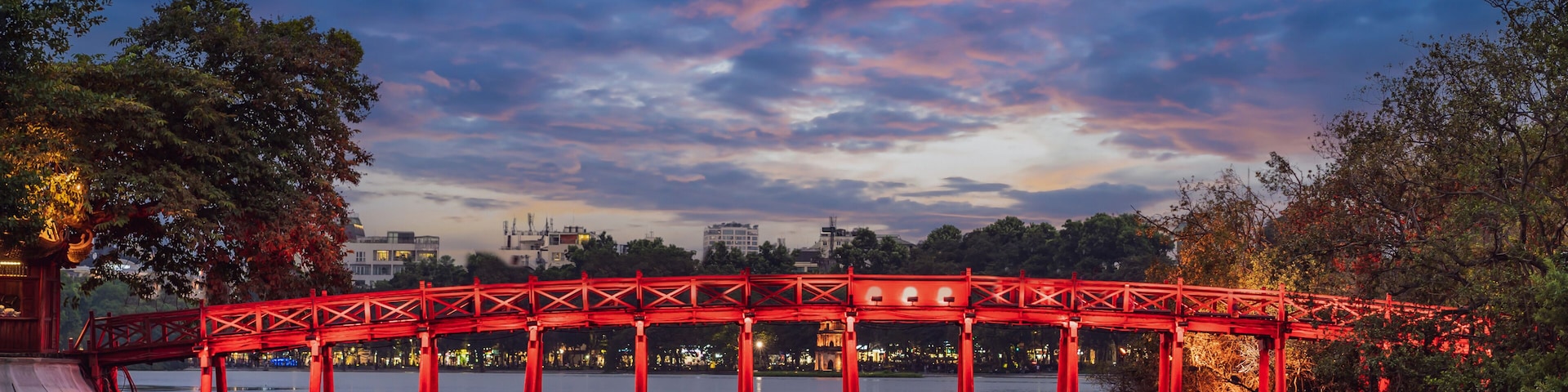 Uma ponte vermelha sobre a água, com o horizonte urbano ao fundo.