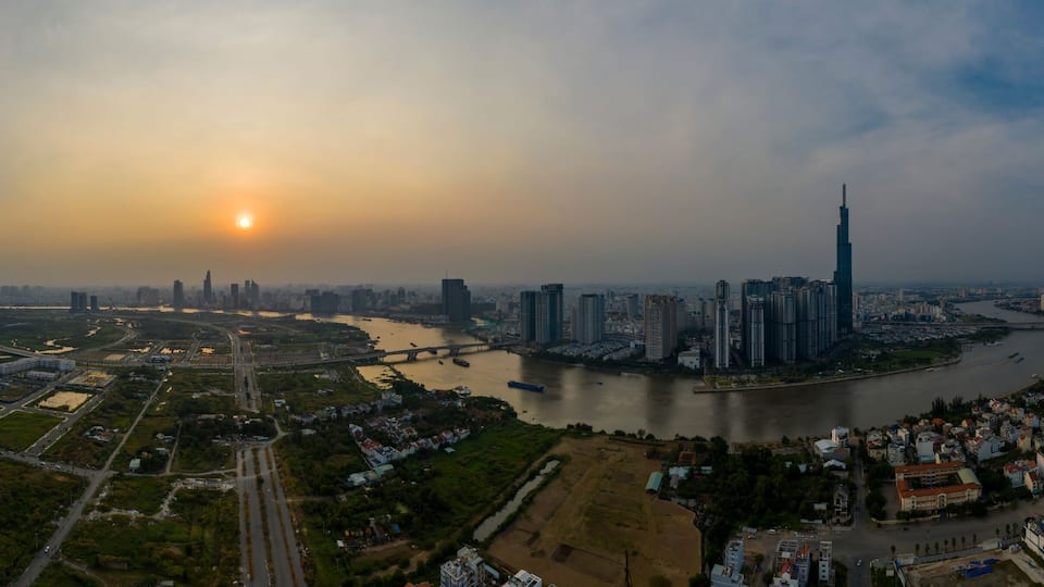 A cityscape with a river, a bridge, and the sun setting or rising.
