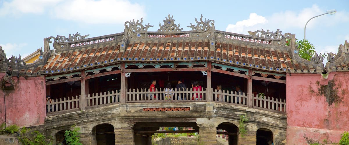 Un puente tradicional con barandillas ornamentadas y un techo de tejas que cruza un canal.