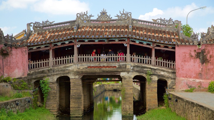 Un pont traditionnel, doté de garde-corps décoratifs et d’un toit recouvert de tuiles, enjambant un canal.