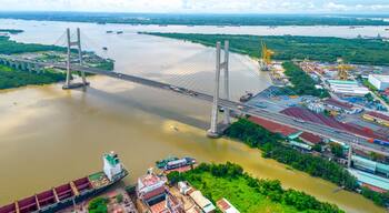 Un grand pont suspendu enjambant une rivière, avec des navires de transport de marchandises et des bâtiments industriels à proximité.