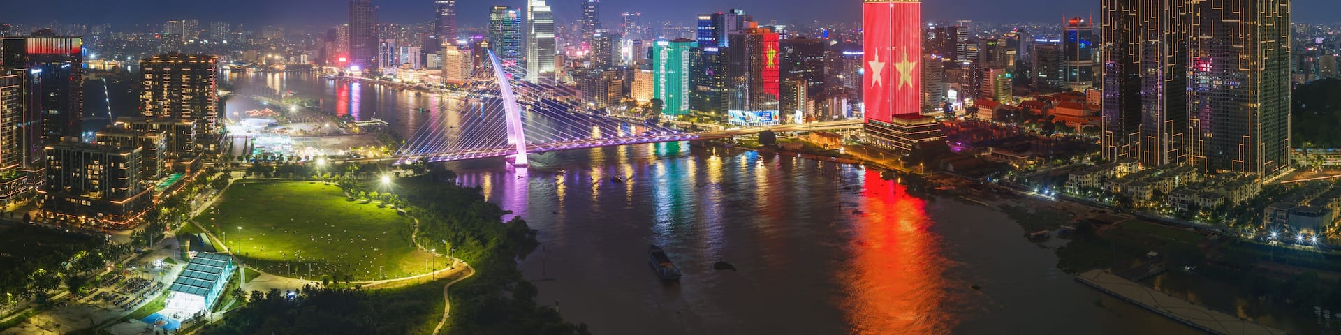 HO CHI MINH CITY, VIETNAM: Aerial view of Ba Son bridge and city center skyline illuminated with red national flag LED light at night