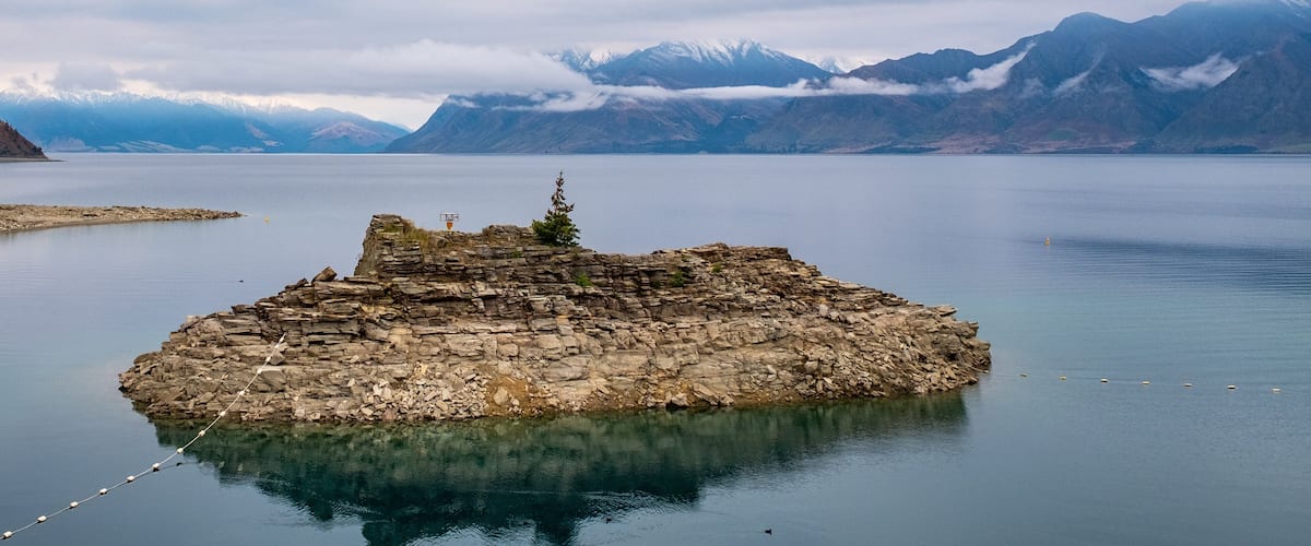A rocky island in a calm lake with mountains in the background.