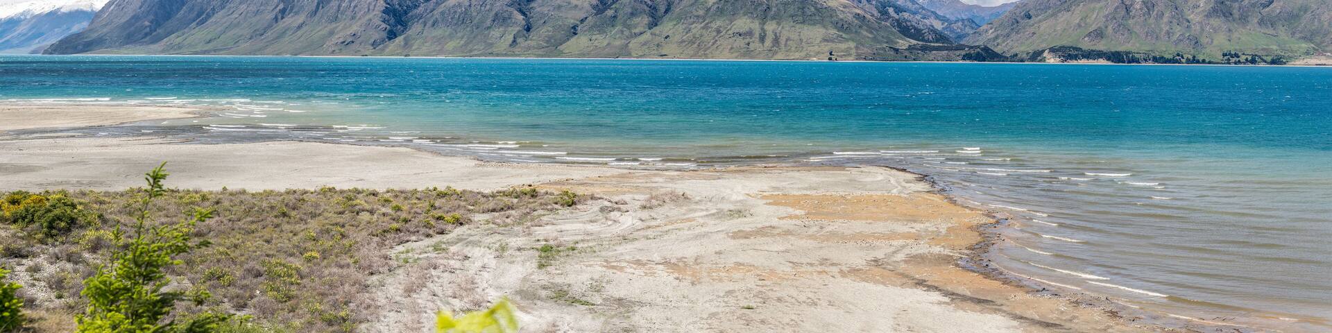 A coastal landscape with mountains in the background and a clear blue sea.