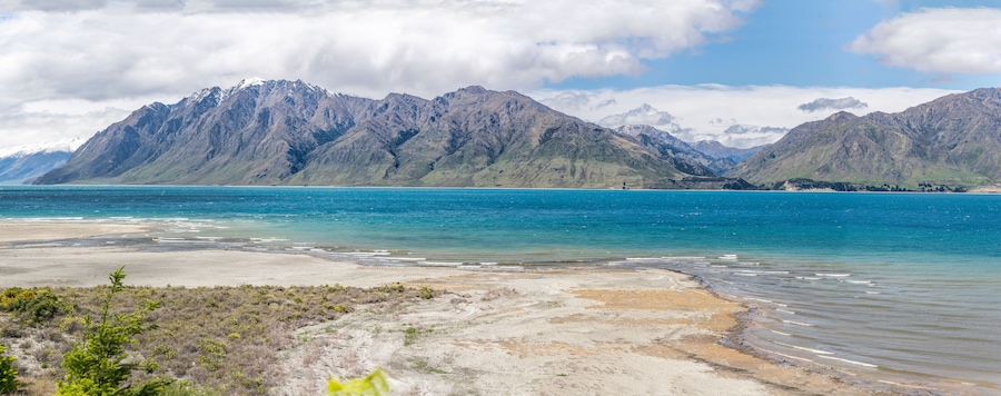 A coastal landscape with mountains in the background and a clear blue sea.
