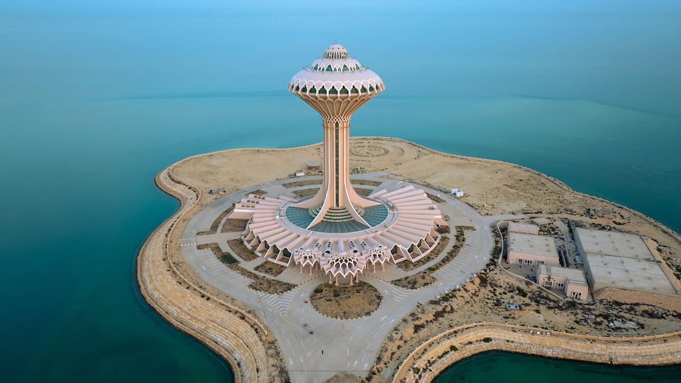 A unique tower structure surrounded by a circular road and a beach.