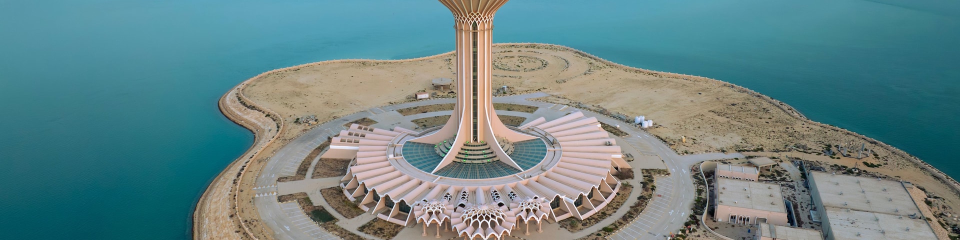 Estrutura de torre singular, cercada por uma estrada circular e uma praia.