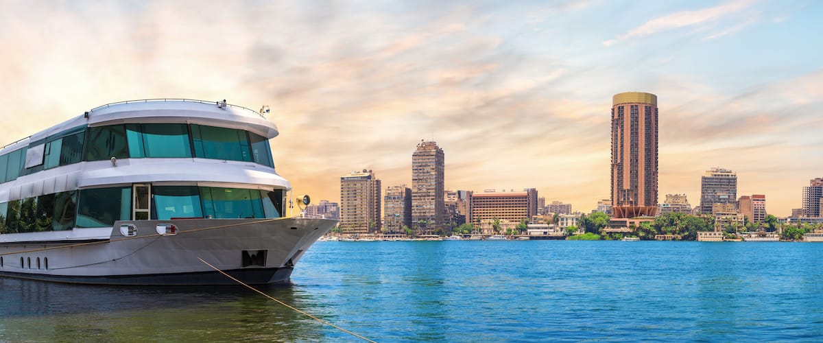 A large yacht docked near a city skyline with modern buildings and a clear sky.