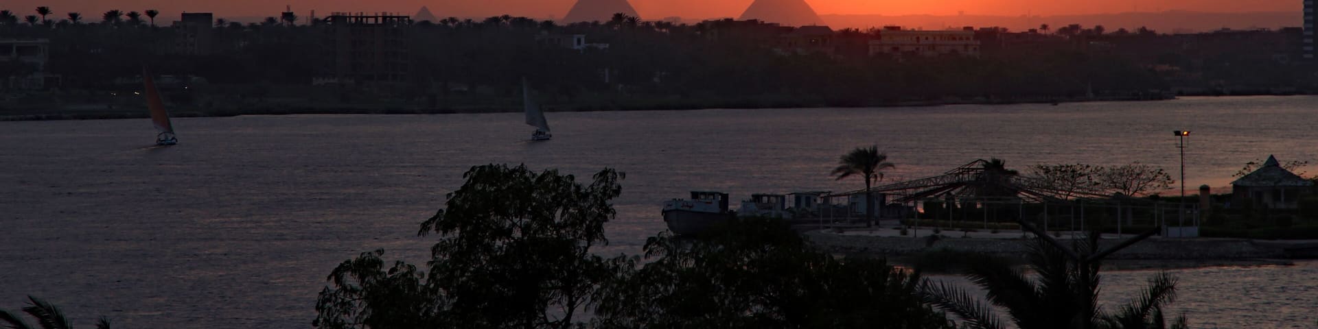 Dramatic fiery red and orange sunset over the River Nile with feluccas calmly sailing and the magnificent Giza pyramids in the background. View from Maadi, Cairo, Egypt.